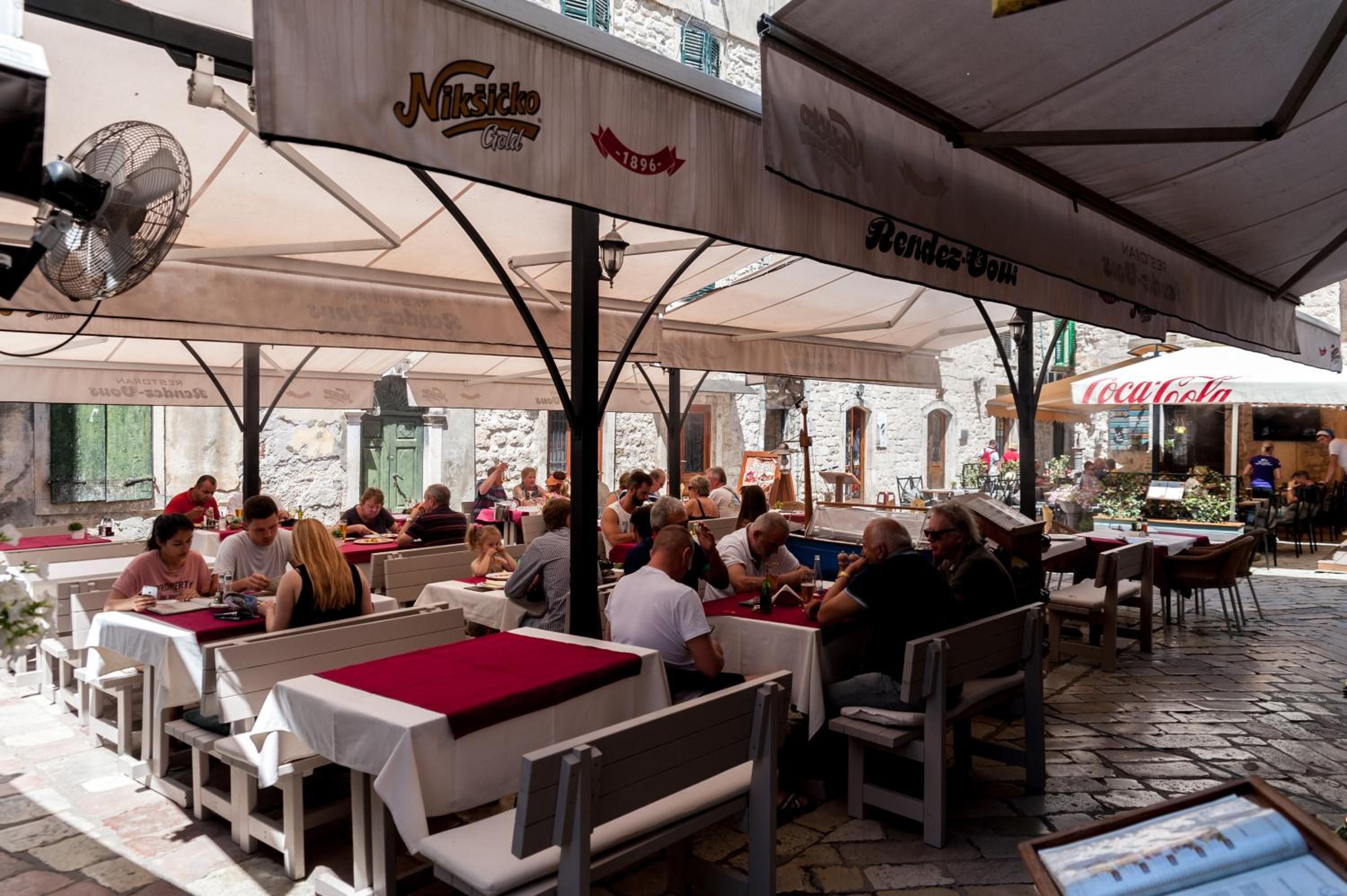 An outdoor café with tables and chairs under umbrellas, with people dining.
