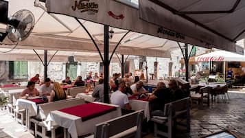 Ein Café im Freien mit Tischen, Stühlen und Sonnenschirmen, an dem Gäste speisen.