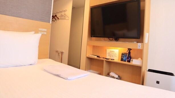 A hotel room with a bed, a television mounted on the wall, a small shelf with items, and a door leading to another room. - Hotel Passage 2 (Aomori)