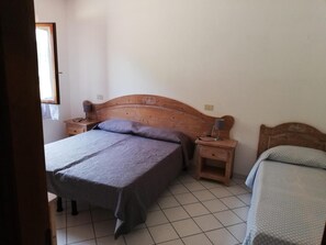 A bedroom with a wooden bed, two bedside tables, and a tiled floor. - Il Castagno (Marciana)