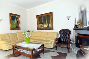 A living room with a beige sofa, a black armchair, a coffee table with a vase of flowers, and two framed paintings on the wall. - Kyridis Hotel (Komotini)