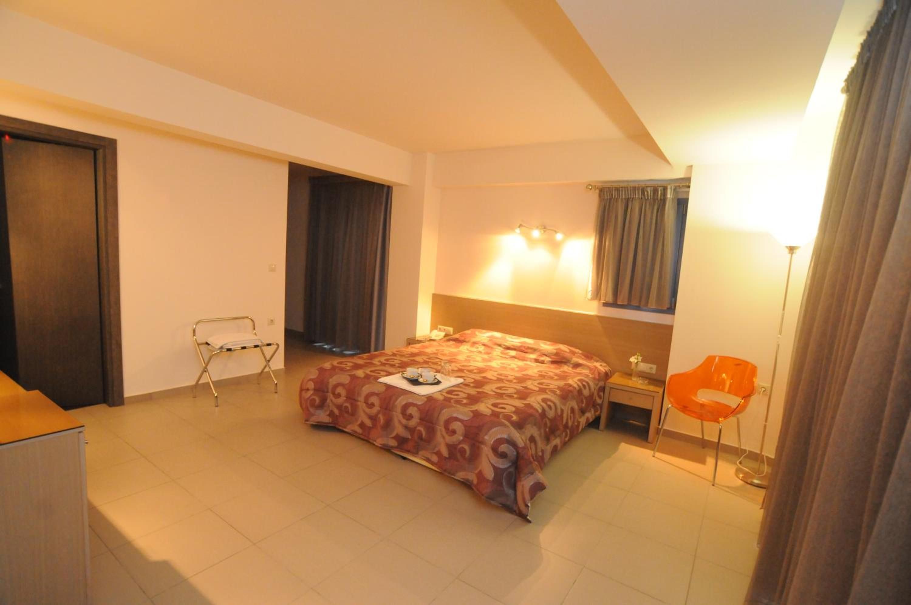 A hotel room with a bed, a chair, a desk, and a lamp.