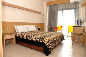 A hotel room with a bed, a desk with a chair, a TV, and a window with curtains. - Kyridis Hotel (Komotini)