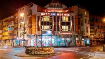 Ein mehrstöckiges Gebäude mit einem auffälligen 'HOTEL HERMES'-Schild, einem 'Supermarkt'-Schild und einem 'Placinte'-Schild.