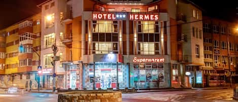 En byggnad med flera våningar, med en tydlig skylt som visar texten ”HOTEL HERMES”, en skylt med texten ”Supermarkt” och en skylt med texten ”Placinte”.