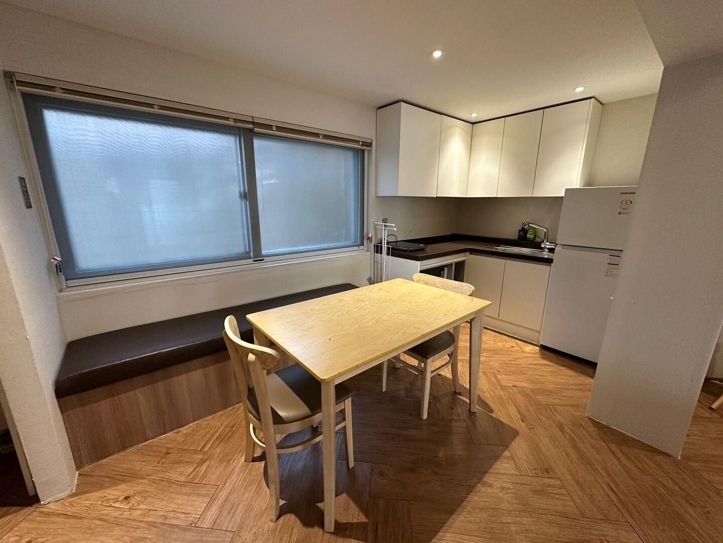 A compact kitchen with a dining table, bench seating, and a refrigerator.