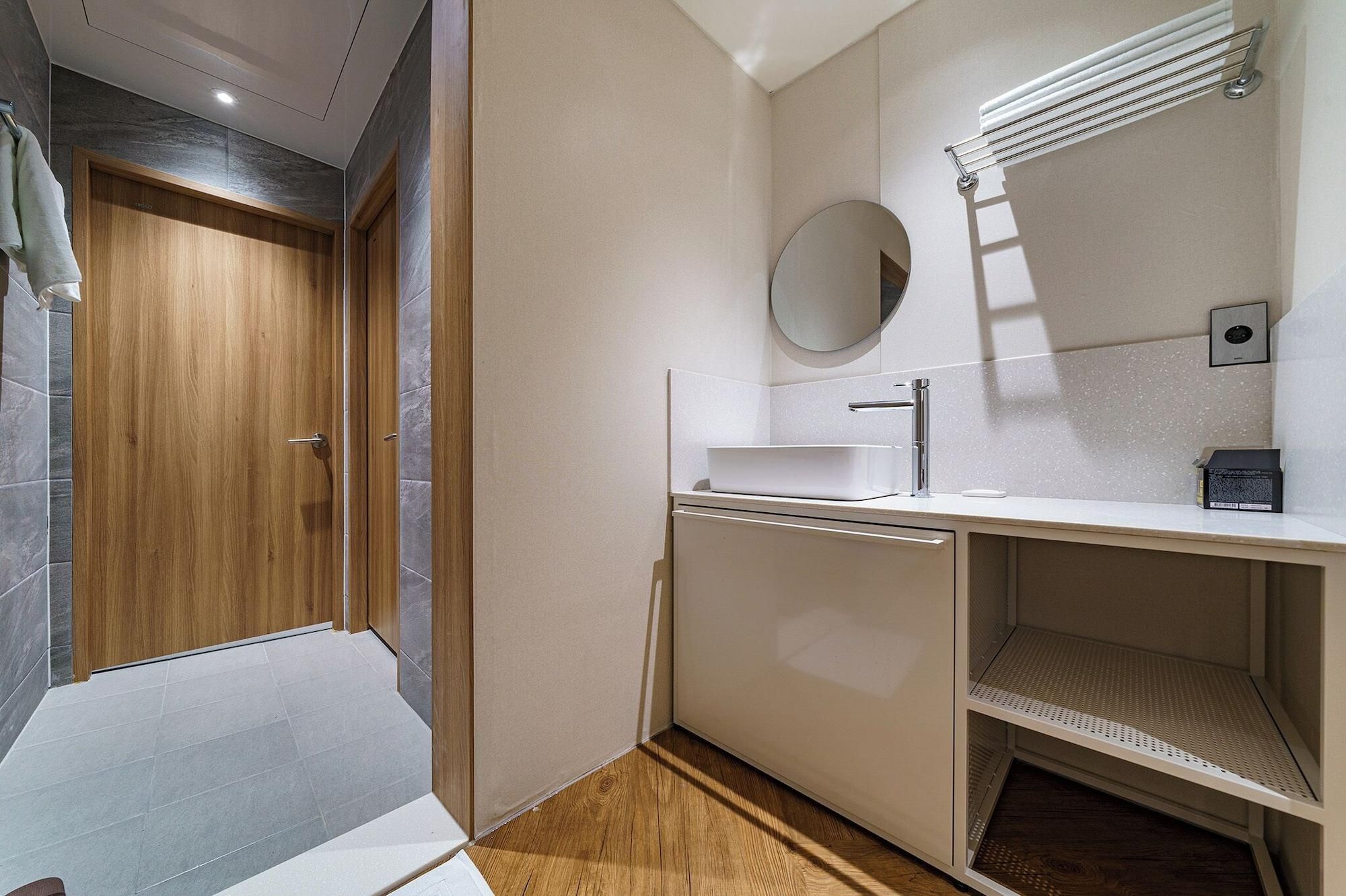 A modern bathroom with a wooden door, a white sink, a mirror, and a towel rack.