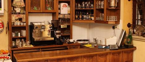 A bar area with wooden cabinets stocked with bottles, a coffee machine, and stools.