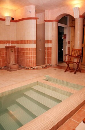 A spa area with a tiled pool, a wooden chair, and a door leading to another room. - Lv Vay Villa Hotel (Miskolc)