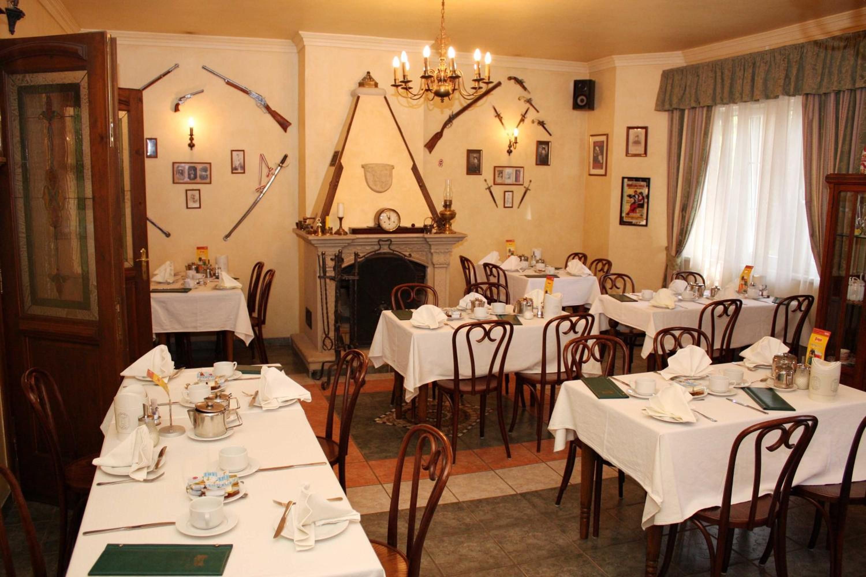 A dining room with multiple tables set for service, a fireplace, and wall-mounted weapons.