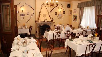 A dining room with multiple tables set for service, a fireplace, and wall-mounted weapons.