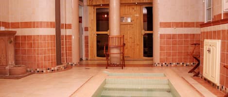 Un espacio de spa con suelo de baldosas, una silla de madera y una pequeña piscina.