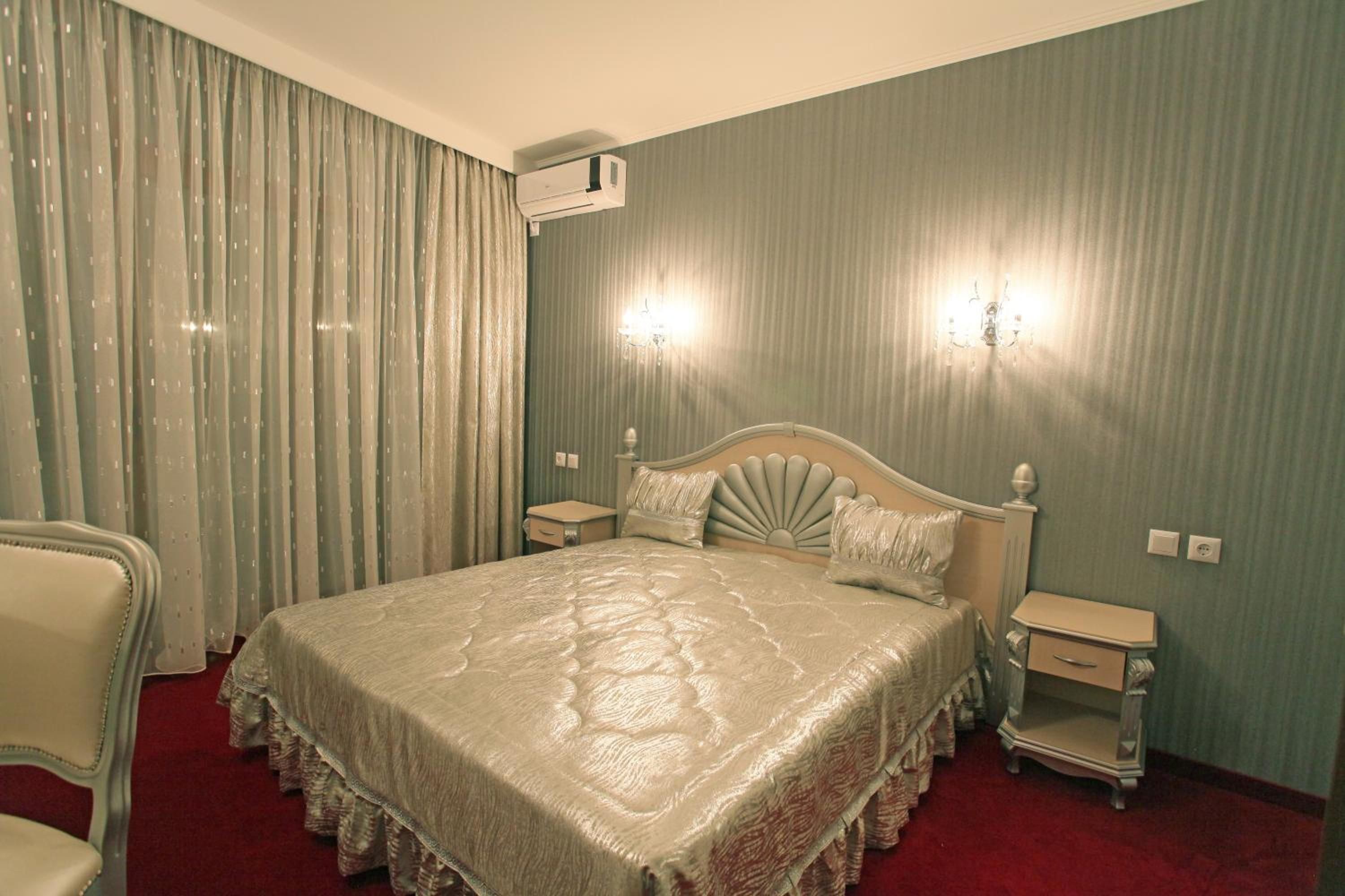 Una habitación de hotel con una cama grande, dos mesitas de noche, una silla, un equipo de aire acondicionado y una araña.