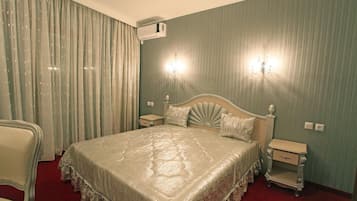 Una habitación de hotel con una cama grande, dos mesitas de noche, una silla, un equipo de aire acondicionado y una araña.