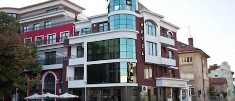 A multi-story hotel with a prominent corner tower, large windows, and outdoor seating.