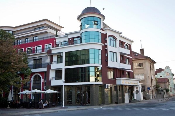 A multi-story hotel with a prominent corner tower, large windows, and outdoor seating.