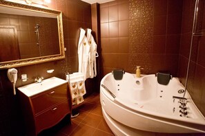 A bathroom with a large bathtub, a vanity with a mirror, and a hairdryer. - Hotel Diamond (Kazanlak)
