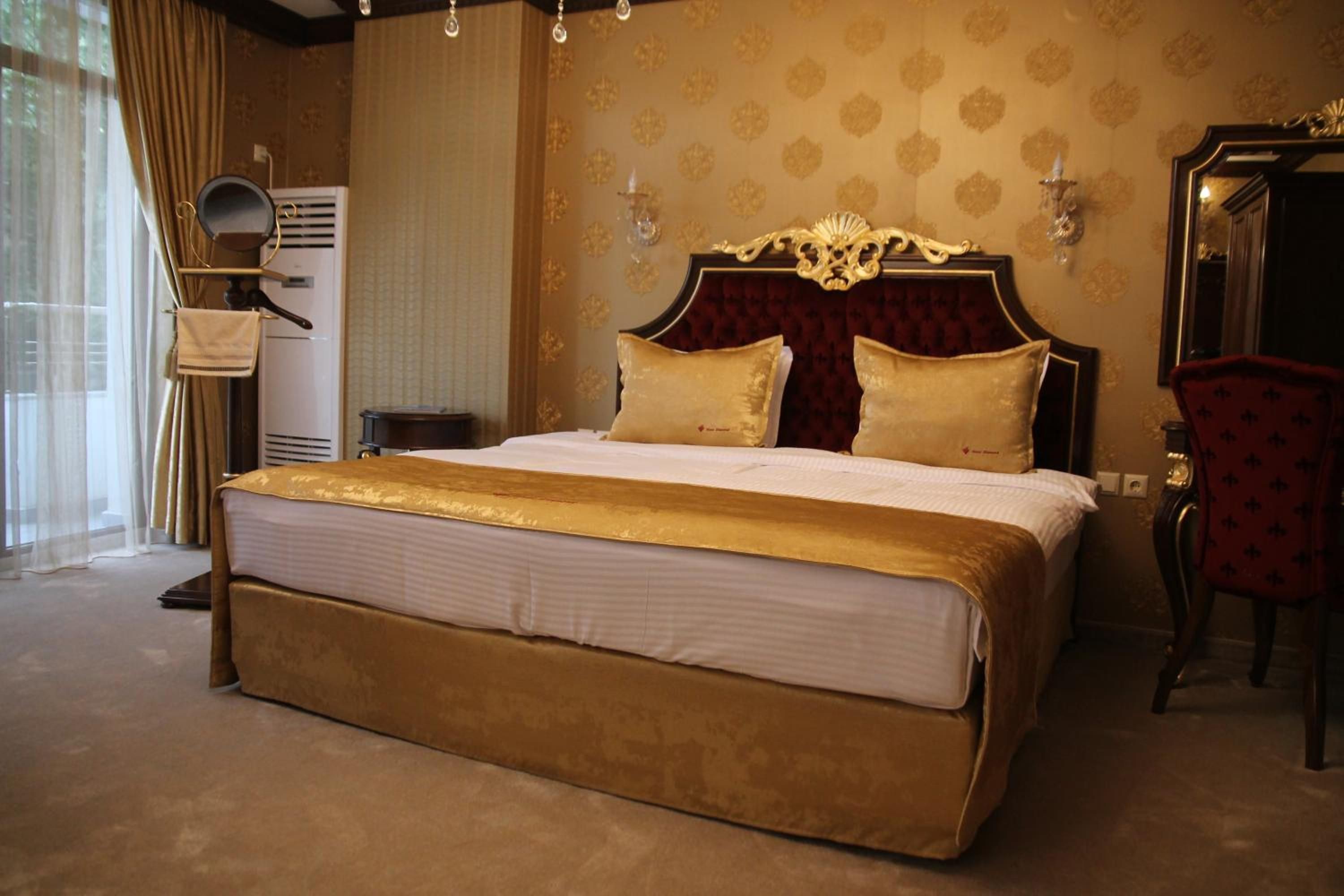 Una cama grande con cabecera dorada y dos almohadas, una silla roja y un espejo en la pared.