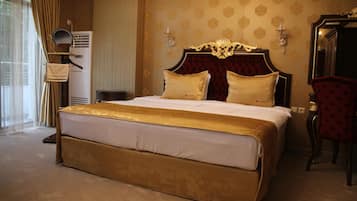 Una cama grande con cabecera dorada y dos almohadas, una silla roja y un espejo en la pared.
