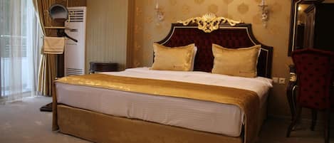 Una cama grande con cabecera dorada y dos almohadas, una silla roja y un espejo en la pared.