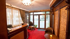 Un vestíbulo de hotel con una recepción, un área de descanso con mesa y sillas, y un ventanal que ofrece vistas al exterior.
