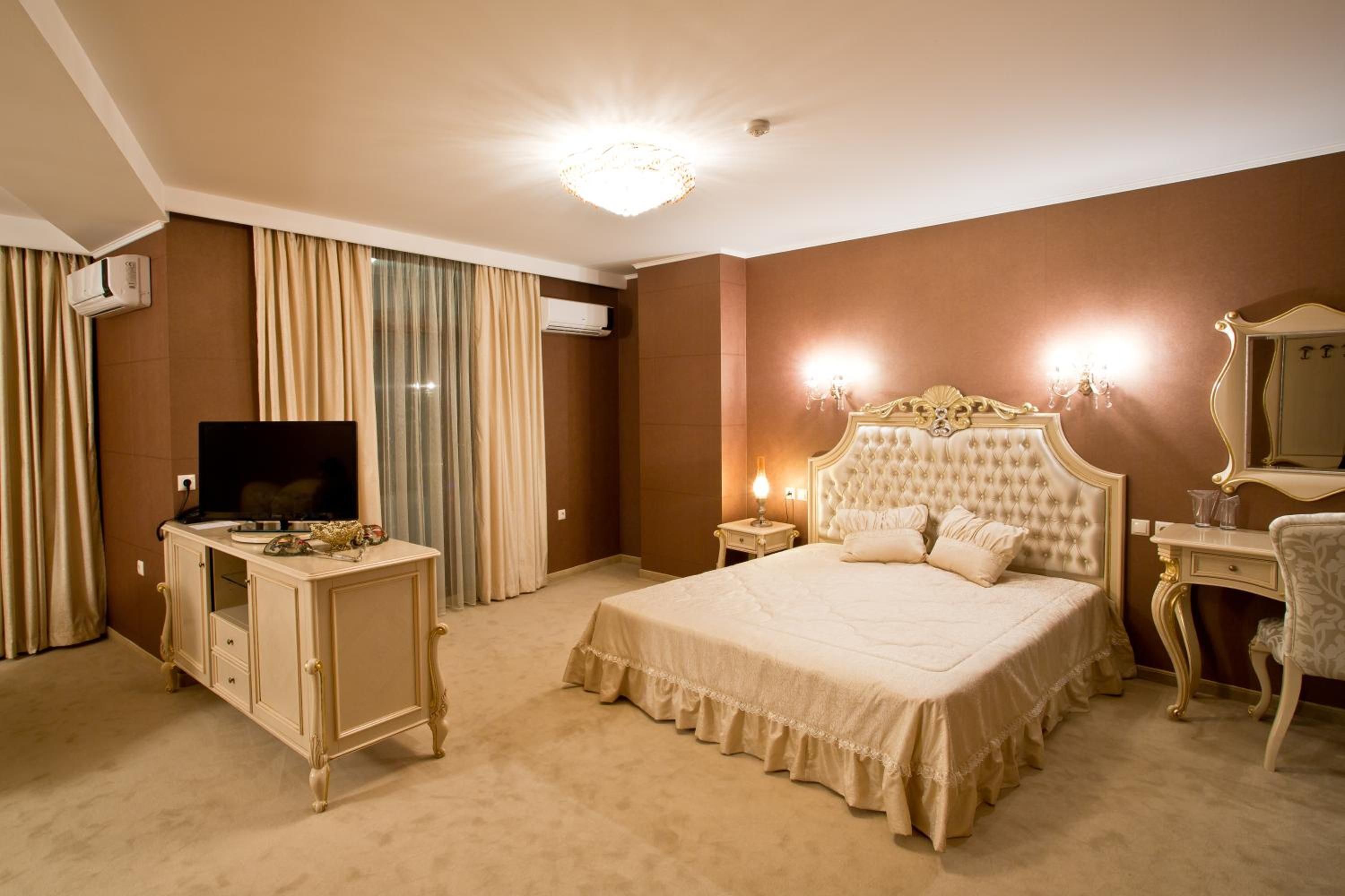 A hotel room with a large bed, a television, a dresser, and an air conditioning unit.