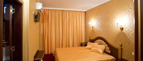 Quarto de hotel com uma cama grande, uma mesa de cabeceira, uma luminária na parede e uma porta com espelho.