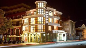 Un hotel de varios pisos con una entrada destacada en esquina, amplias ventanas y terraza al aire libre.