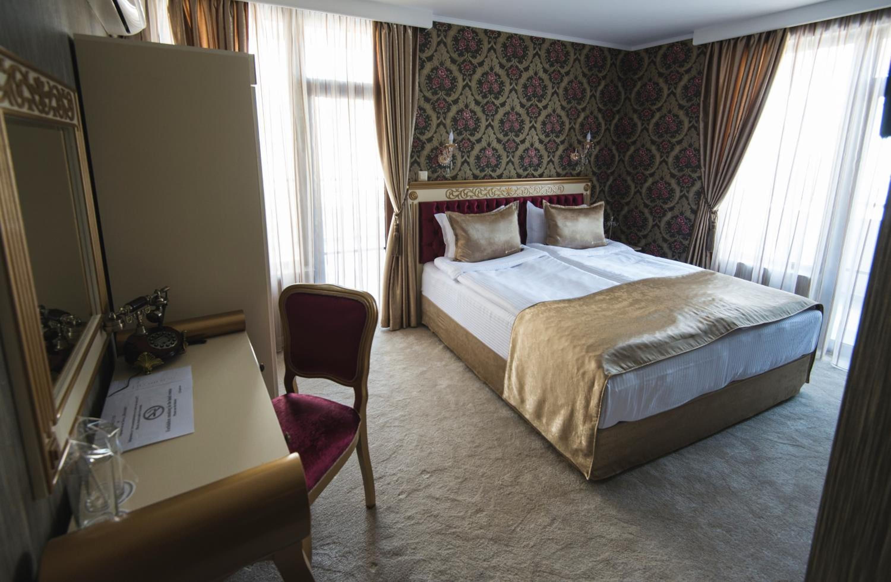 Una habitación de hotel con cama, escritorio con silla, espejo y papel tapiz estampado.
