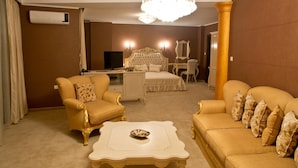 Habitación de hotel con una cama grande, dos sillones, un escritorio, un televisor y una araña.