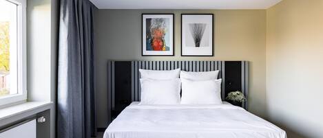 Una habitación de hotel moderna con una cama grande, cortinas grises y dos cuadros enmarcados en la pared.