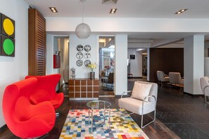 A modern interior with a red chair, a beige armchair, and a patterned rug. - Numa I Bona Rooms Apartments (Bonn)