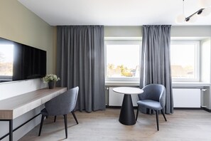 A modern living room with a flat-screen TV, two grey chairs, a small round table, and a window with grey curtains. - Numa I Bona Rooms Apartments (Bonn)