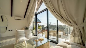 A modern living room with a glass coffee table, white sofas, and a large window with curtains. - VIlla Ezra Azul (Uluwatu)