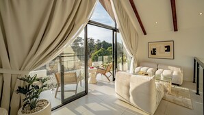 A modern living room with a large glass door leading to a balcony, a white sofa, a glass coffee table, and a framed artwork on the wall. - VIlla Ezra Azul (Uluwatu)