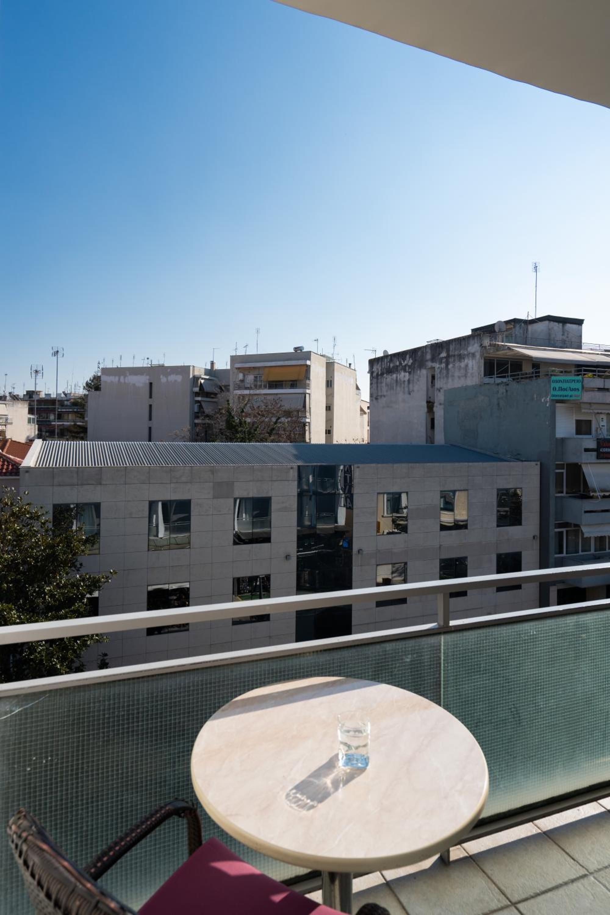 A balcony with a round table and a chair, overlooking a cityscape with buildings.