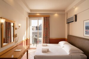 A hotel room with a bed, a desk, a mirror, a phone, and a window with curtains.