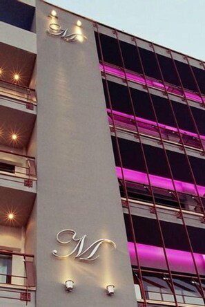 Un edificio con un llamativo letrero vertical que presenta una 'M' estilizada y una serie de luces a lo largo de su fachada.
