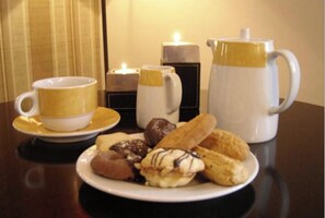 Una mesa con una taza de café, un plato de pasteles, una vela y una cafetera.