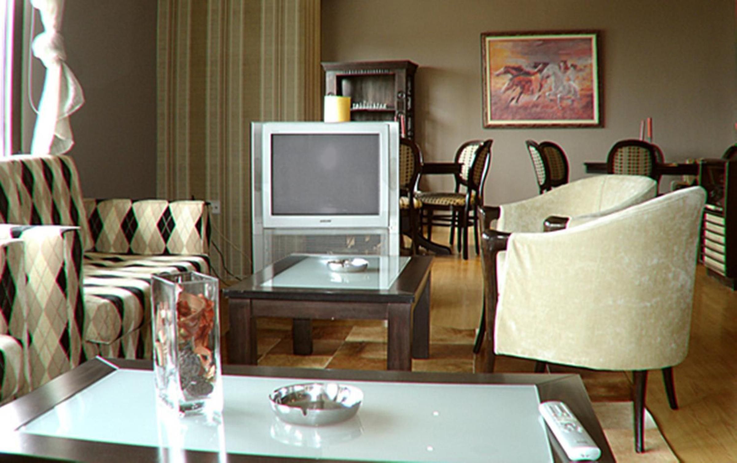 Ein Wohnzimmer mit Fernseher, Sitzgelegenheiten und einem Gemälde an der Wand.