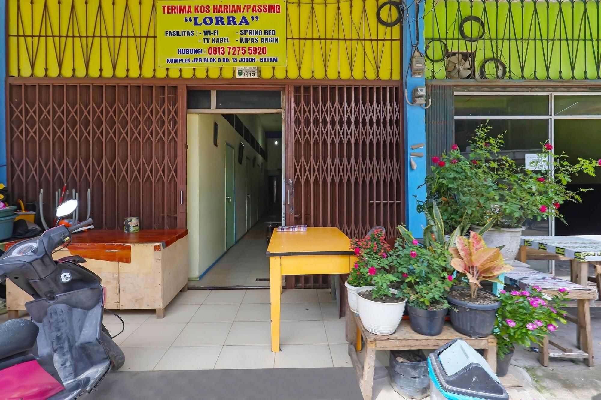 A storefront with a yellow signboard, a wooden table, potted plants, and a scooter outside.