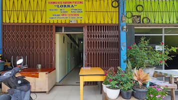 A storefront with a yellow signboard, a wooden table, potted plants, and a scooter outside.