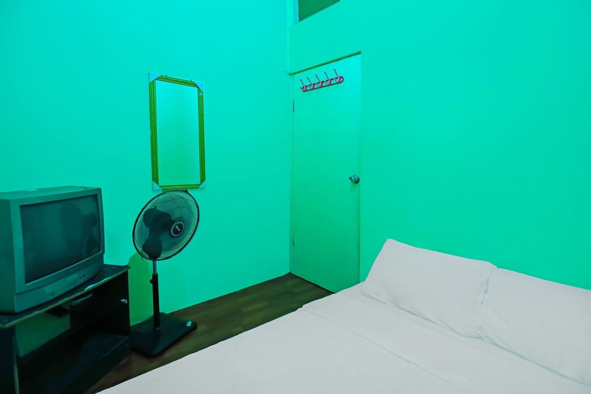 A room with a bed, a television, a fan, and a door with a sign.