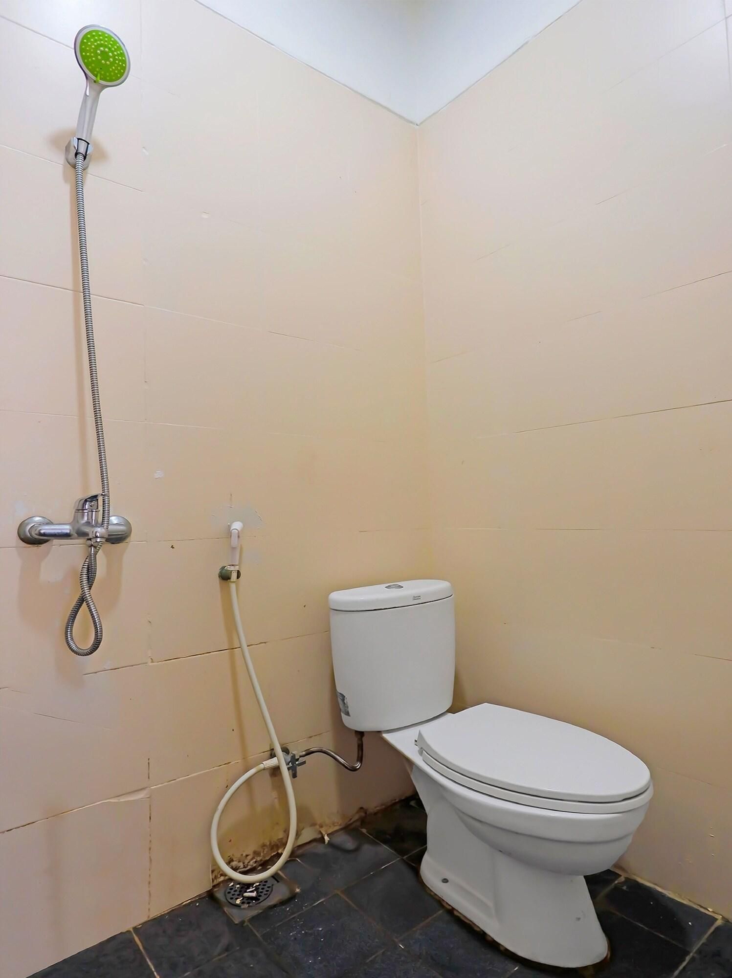 A small bathroom with a toilet, a shower head, and a toilet paper holder.