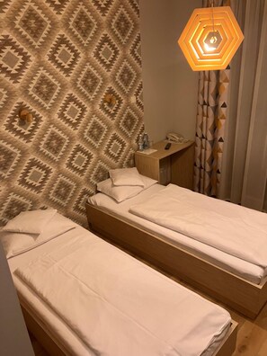 A hotel room with two single beds, a wooden nightstand, a telephone, and a geometric patterned wall. - Hotel Vis A Vis (Olesnica)