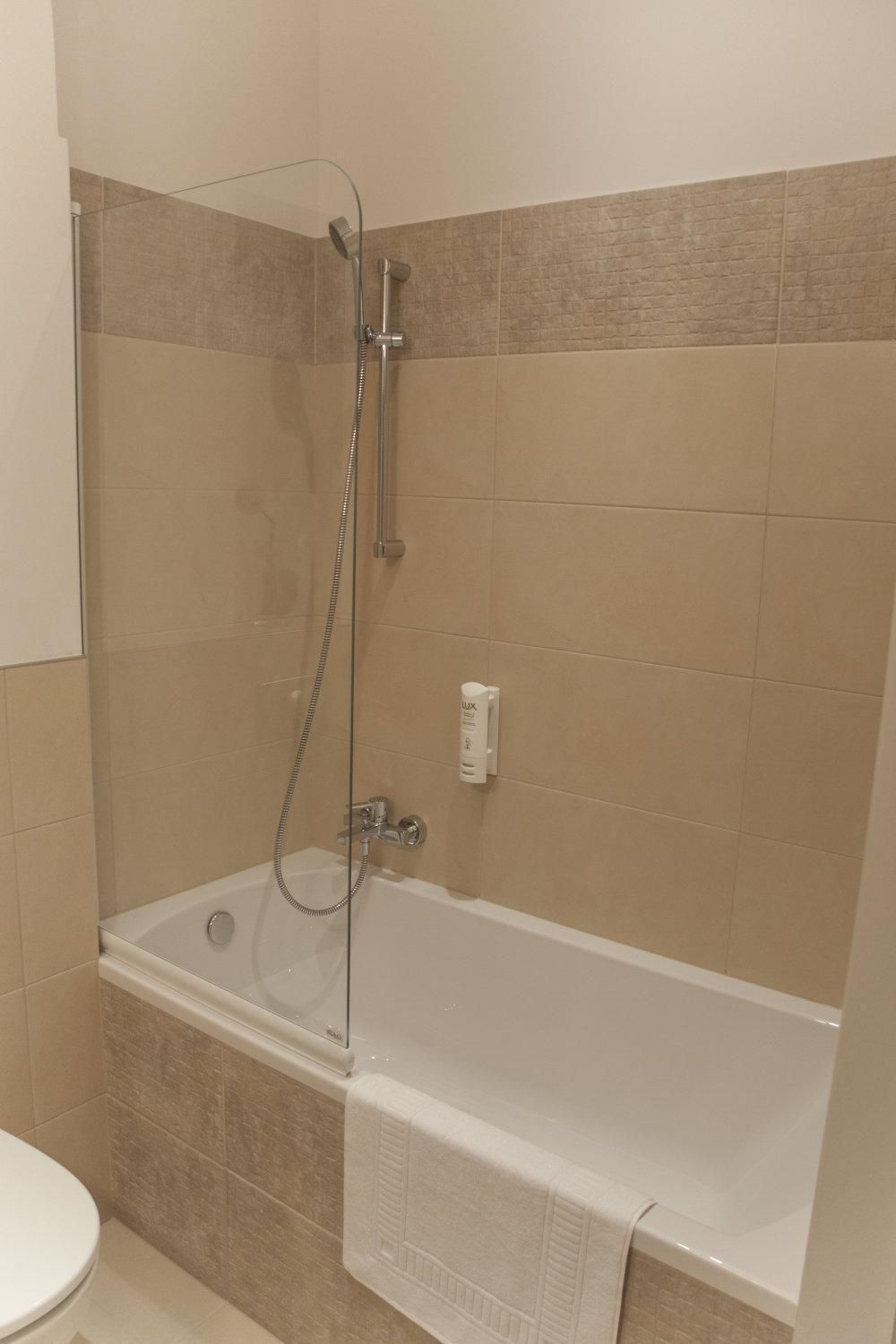 Ein Badezimmer mit einer gläsernen Duschkabine, einer weißen Badewanne und beigen Fliesen.