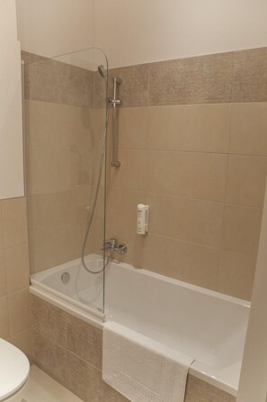 A bathroom with a glass-enclosed shower, a white bathtub, and beige tiles. - Hotel Vis A Vis (Olesnica)
