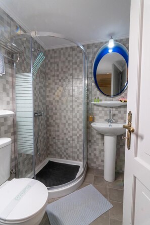 Een badkamer met een glazen douchecabine, een witte wastafel en een toilet.