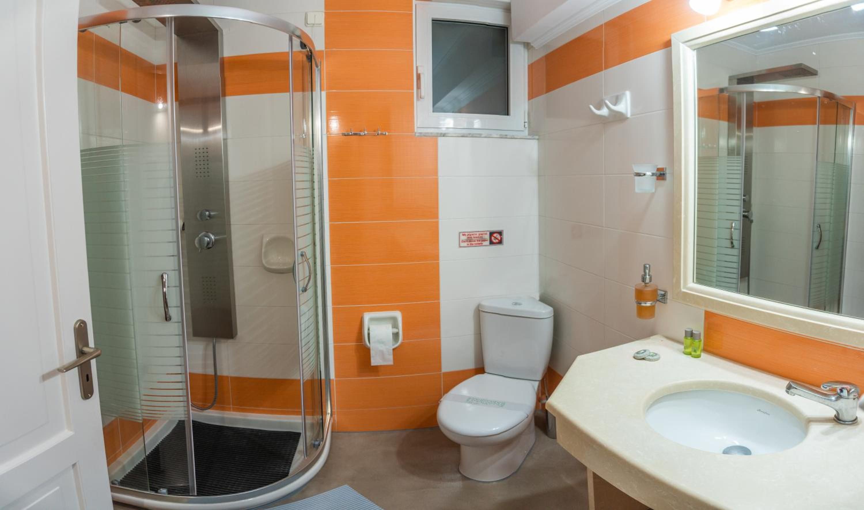 A bathroom with a glass-enclosed shower, a toilet, and a sink with a mirror.