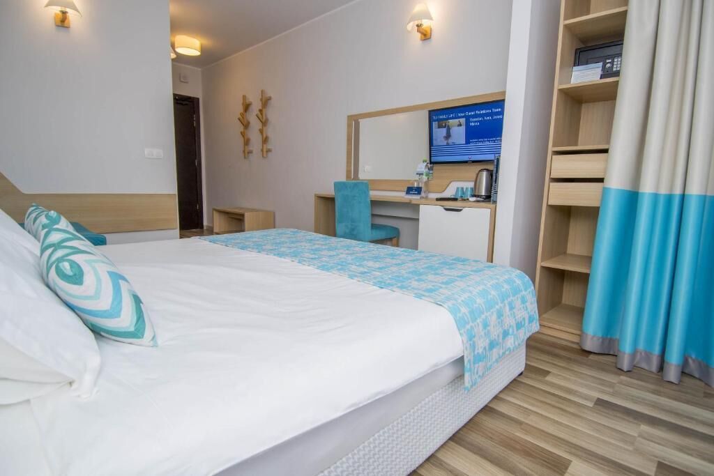 A hotel room with a bed, a desk, a chair, a television, and a wardrobe.